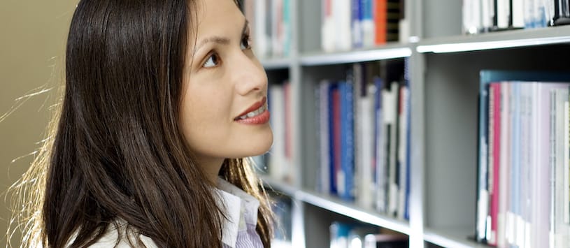 A woman in a library looking up at a row of books. If you want to train for a health sciences career contact NWSC.